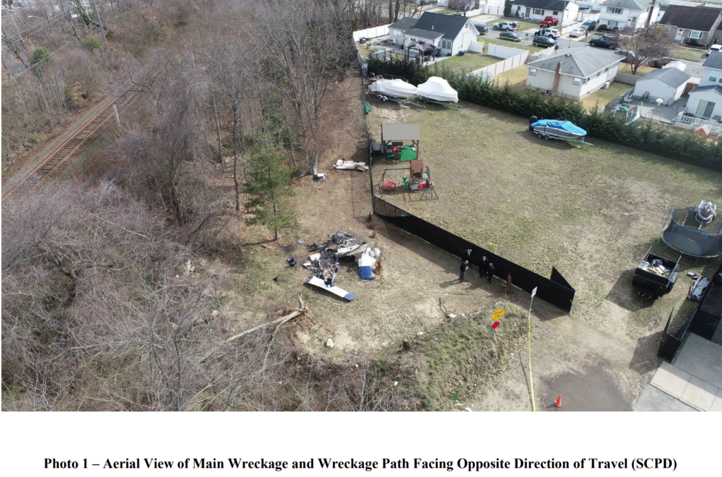 An aerial view of the crash site showing the main wreckage in a backyard area, with burned debris, trees, and nearby houses. Investigators are seen examining the scene.