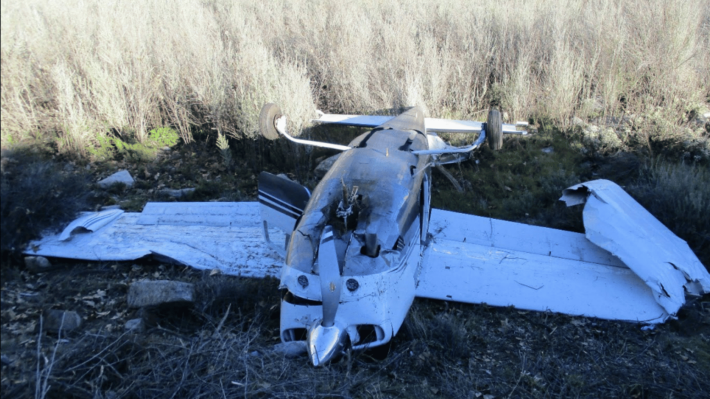 The wreckage of a Cessna T210N, registration N4758C, is seen upside down in a field.