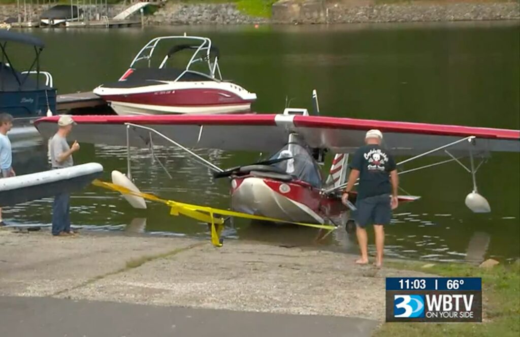 Amphibious Searey aircraft being towed from a lake onto a boat ramp by several people after a water landing incident.