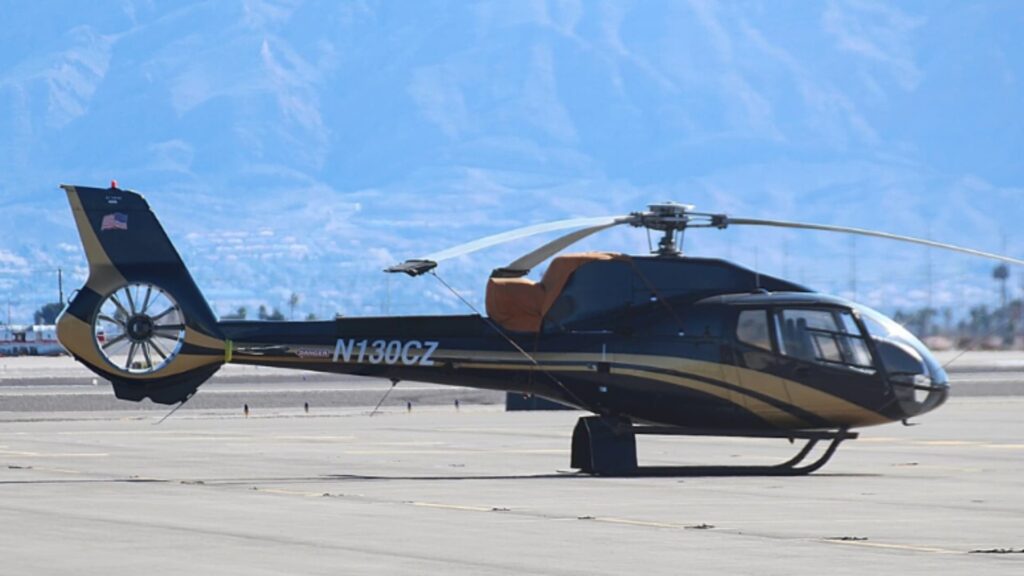 A black and gold Airbus Helicopters EC130B4 with registration N130CZ parked on an airport tarmac with mountains visible in the background.
