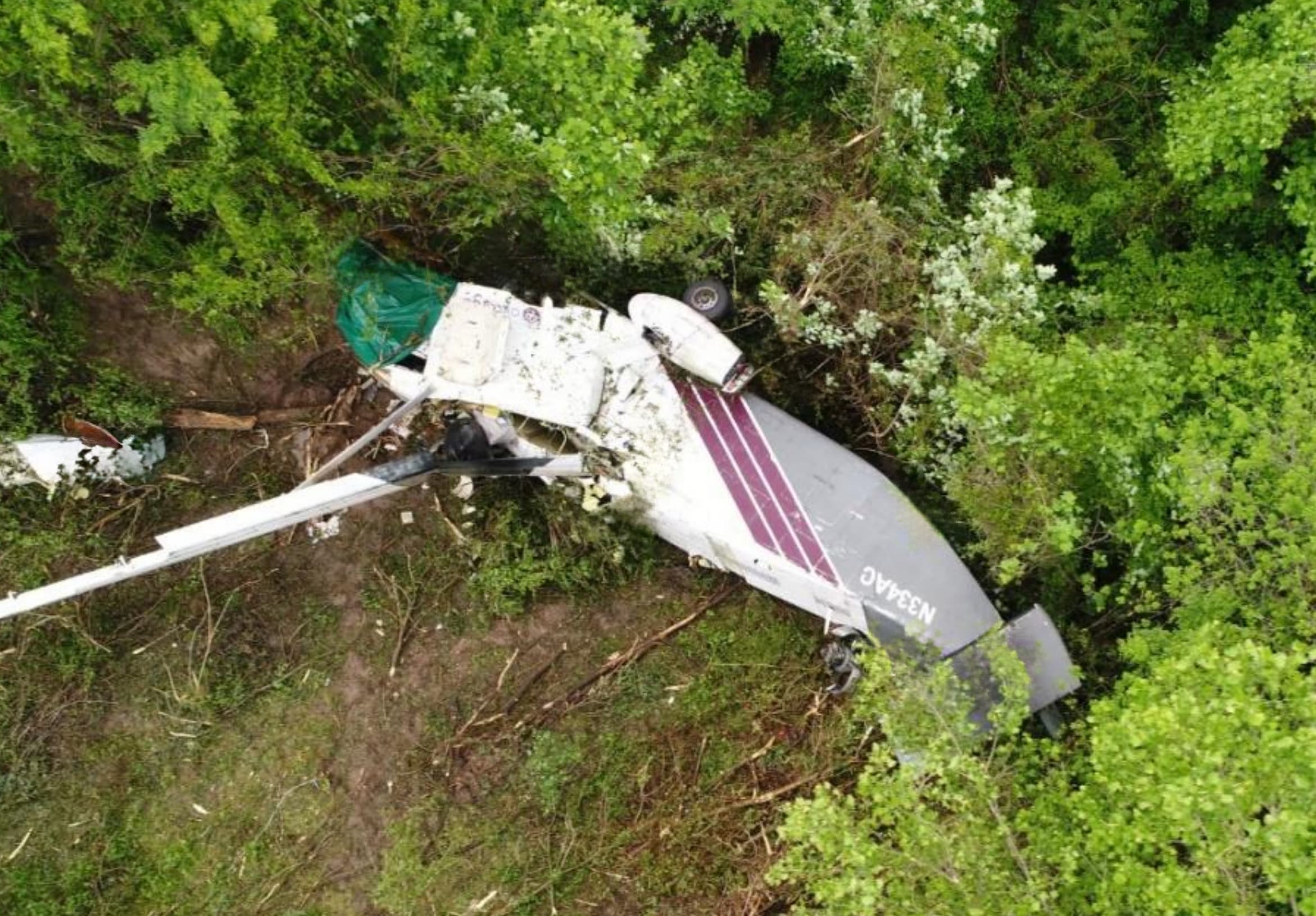 erial view of the wreckage of a white and maroon Shorts SD3-30 aircraft (tail number N334AC) lying in a wooded area, with the left wing torn off and surrounded by broken trees and debris from the crash.