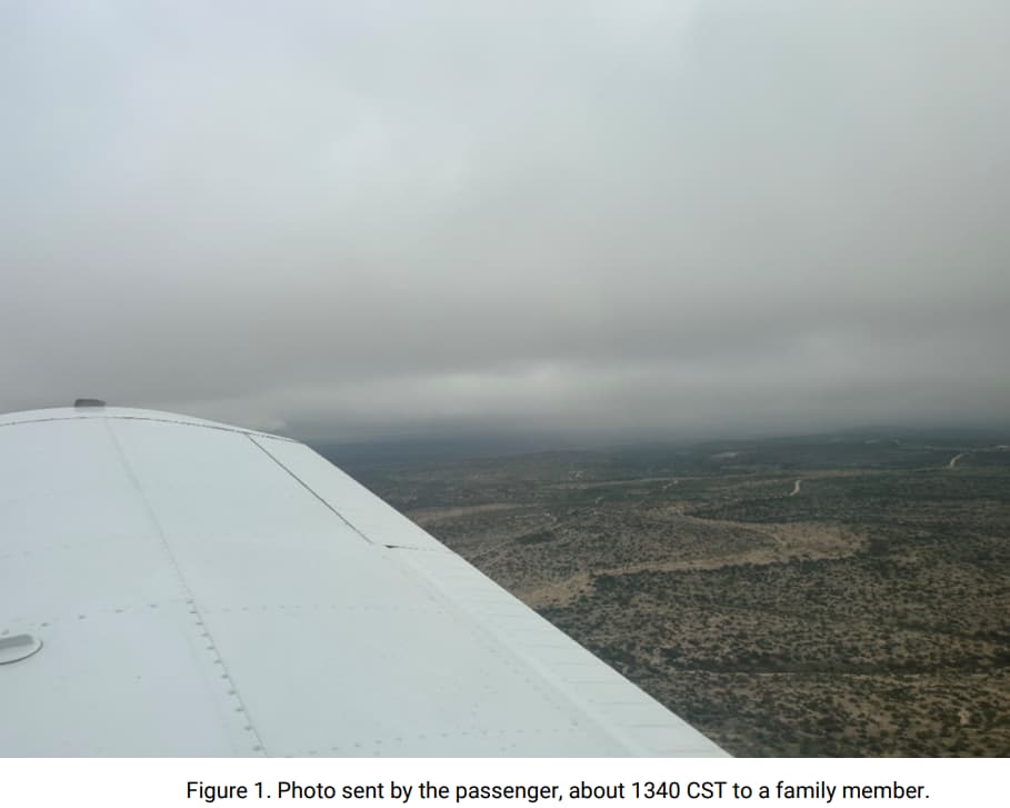 View from an airplane wing looking out over a sparsely vegetated landscape under overcast skies. The wing dominates the left side of the frame, and low clouds are visible ahead, obscuring the horizon. Photo was taken at approximately 1340 CST by a passenger and sent to a family member.