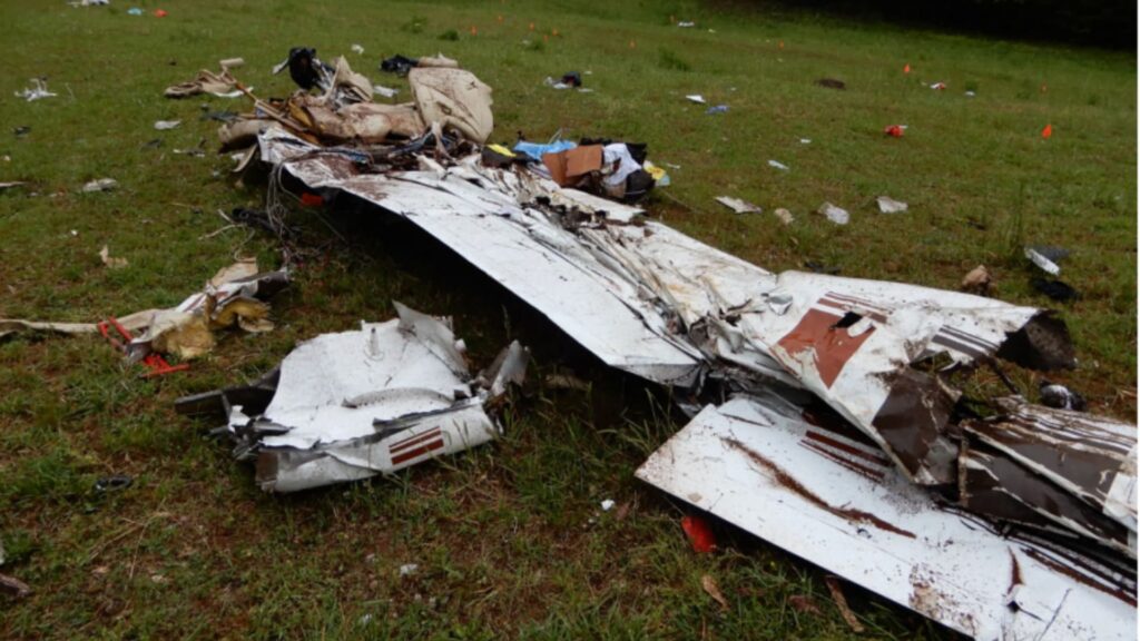 Wreckage of Cessna 177B N123DS in open farm field near Watkinsville, GA, showing fragmented fuselage and wing debris scattered across grassy terrain after in-flight breakup.