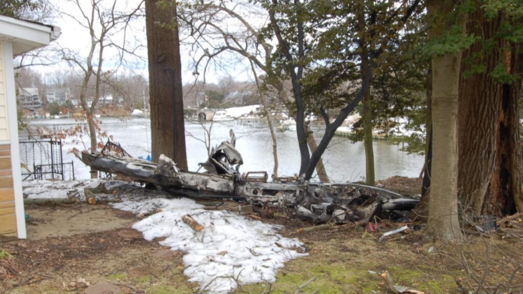 Burned fuselage of Beech P35 Bonanza N1521S lying near trees by a waterfront home in Edgewater, Maryland, after the February 2010 crash.