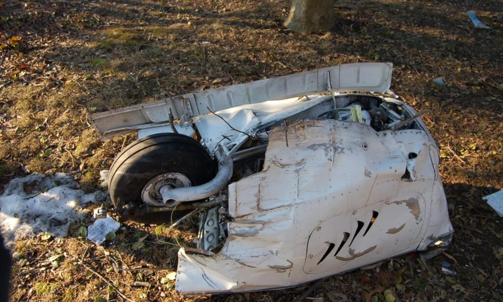 Crashed landing gear assembly separated from the airplane and lying on the ground with visible damage.