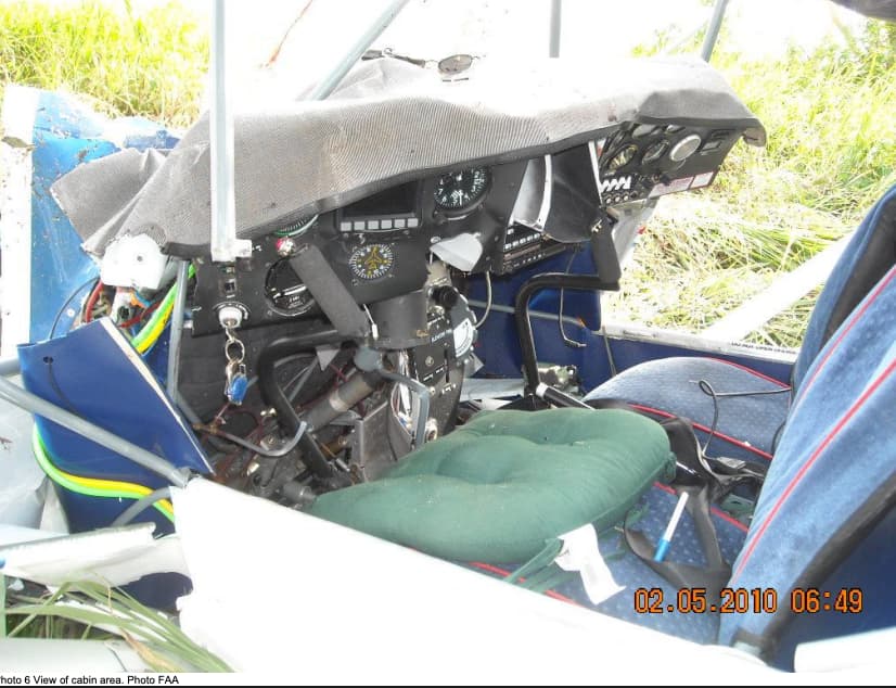 Interior shot of the cockpit, instrument panel pushed inward with broken gauges, wires hanging loose, and the pilot’s seat still in place.