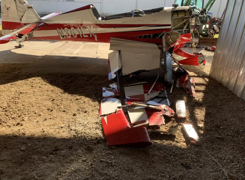 The tail section of the Extra EA300/LC, marked N361LX, stored indoors after recovery; the rear fuselage and control surfaces show crushing and tearing from impact.