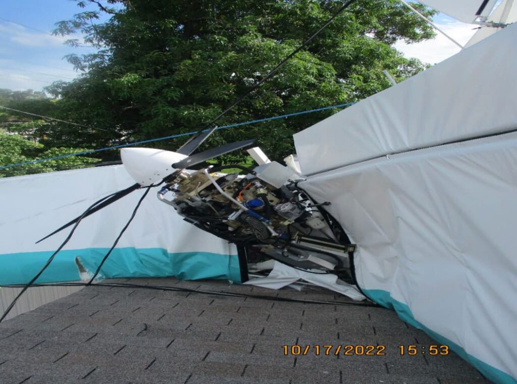 Close-up view of the airplane’s engine and propeller assembly exposed after impact, with surrounding wing structure collapsed onto a roof.