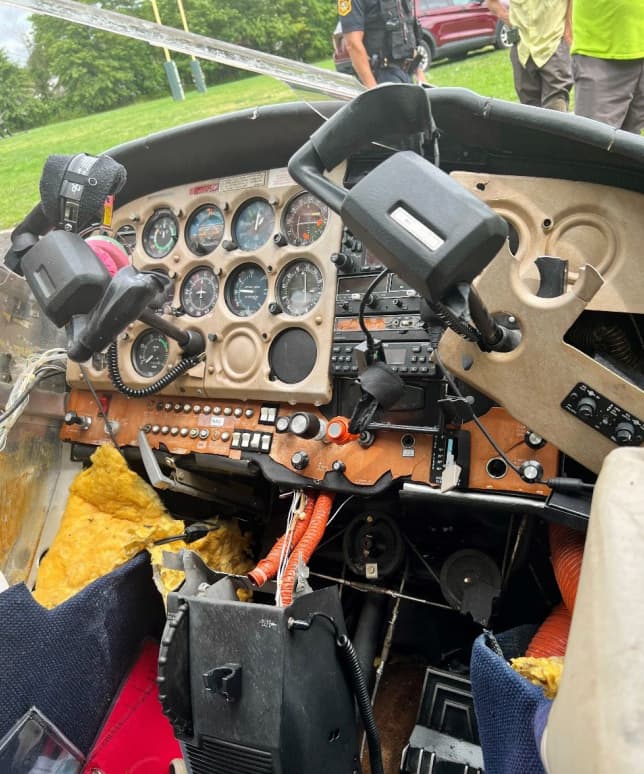 Interior cockpit view of a damaged Cessna 172 showing displaced instrument panel components, exposed wiring, and debris following a hard landing.