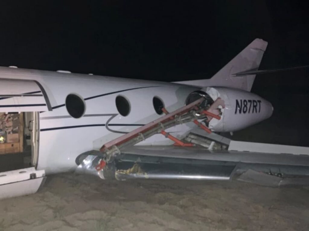 Close-up view of the right wing and collapsed landing gear of Dassault Falcon 10 N87RT following a runway overrun at night.