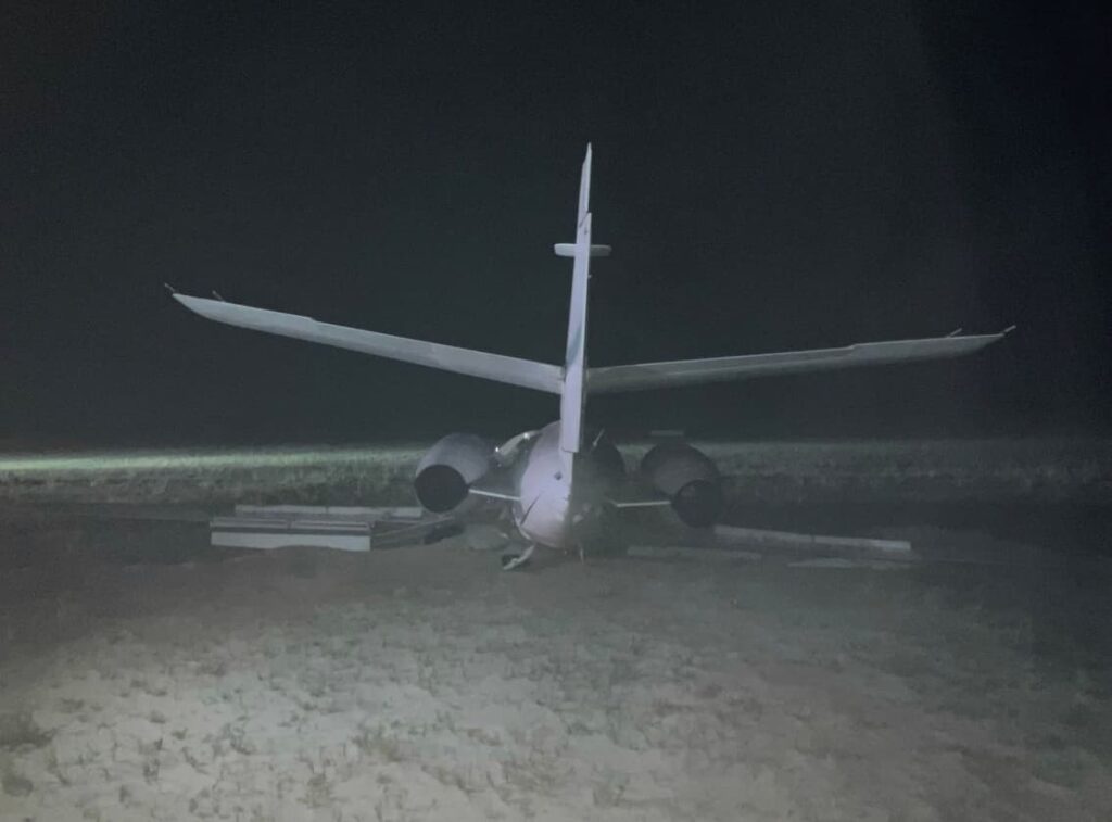 Rear view of Dassault Falcon 10 N87RT after a runway excursion, showing both engines intact and the aircraft settled in soft sand beyond the runway.