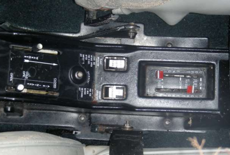 Alt text: Close-up of an aircraft’s center console showing the fuel selector, trim controls, and adjacent switches between the front seats.