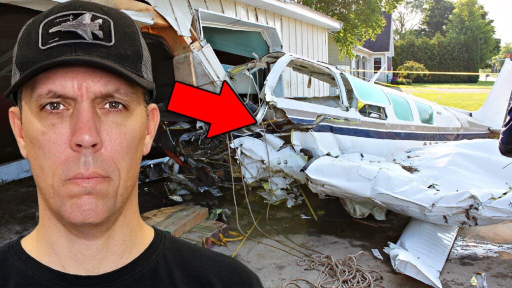 A serious-looking man in a black cap stands in the foreground beside the wreckage of a small airplane that crashed into a building, with a large red arrow pointing toward the damaged aircraft.